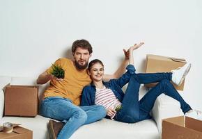 jovem casado casal dentro uma Novo apartamento em uma branco sofá caixas com coisas comovente foto