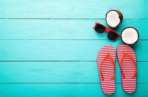 chinelos, óculos de sol e concha do mar sobre fundo azul de madeira. copie o espaço e os acessórios de verão da moda. foto