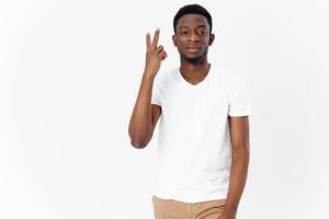 alegre homem africano aparência dentro uma branco camiseta gesticulando com dele mãos moderno estilo luz fundo foto