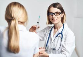 uma mulher médico dentro uma médico vestido é dando a injeção para uma paciente foto