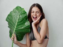 alegre mulher dentro roupa de banho Palma folha segurando a charme do a trópicos foto