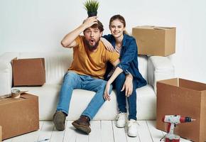 alegre jovem casal dentro a quarto em a sofá com caixas comovente foto