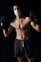 desportivo homem dentro médico mascarar e dentro boxe luvas em Preto fundo calção ginástica modelo pressione foto