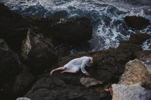 descalço mulher dentro uma branco vestir deitado em uma pedra dentro uma branco vestir inalterado foto