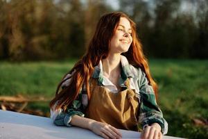 retrato do uma jovem mulher com lindo grandes vermelho cabelo com uma lindo sorrir com dentes contra uma verde parque dentro a verão pôr do sol luz solar foto