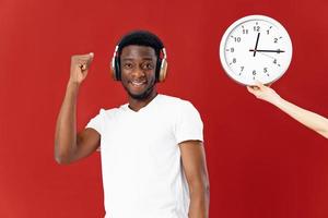 alegre homem do africano aparência dentro uma branco camiseta Próximo para uma relógio em uma vermelho fundo foto