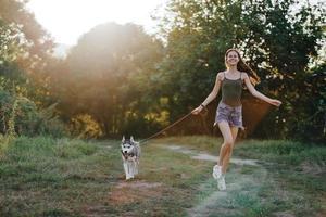 mulher e dela rouco cachorro alegremente corrida através a Relva dentro natureza dentro a parque sorrir com dentes outono andar com bicho de estimação, viajando com uma cachorro amigo foto