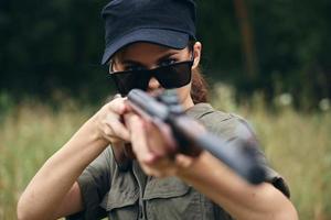 mulher em ao ar livre armas dentro mãos Sombrio óculos Preto boné verde macacão verde foto