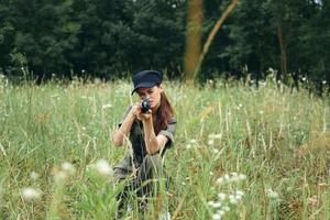 mulher com uma arma visando frente em agachamentos em ao ar livre verde folhas foto