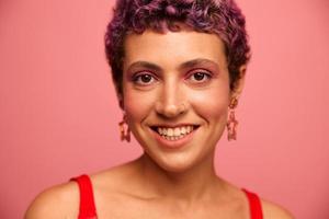 moda retrato do uma mulher com uma curto corte de cabelo do roxa cor e uma sorrir com dentes dentro uma vermelho topo em uma Rosa fundo felicidade foto