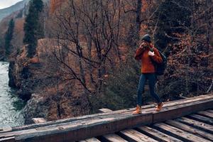 mulher carrinhos em uma ponte sobre uma rio dentro a montanhas outono floresta viagem foto