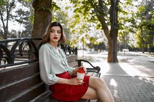 bonita mulher sentado em parque Banco ao ar livre copo do café foto