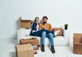 jovem casado casal dentro uma Novo apartamento em uma branco sofá caixas com coisas comovente foto