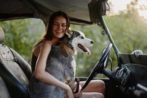 mulher e rouco cachorro alegremente viajando dentro carro sorrir com dentes outono andar com bicho de estimação, viagem com cachorro amigo abraços e danças foto