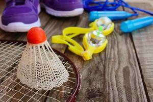 Esportes equipamento a passarinho é em a raquete, saltando corda, natação óculos e tênis em de madeira fundo foto