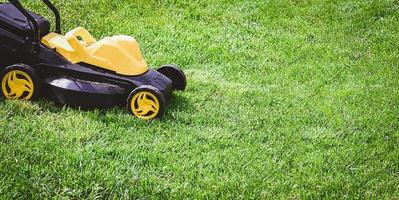 elétrico amarelo e Preto gramado cortador de grama em verde grama, cópia de espaço foto