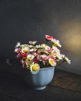 buquê de margaridas comuns no chá cortado na luz brilhante do início da manhã na mesa de madeira foto