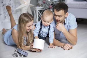 família às Natal com presentes. mãe pai e bebê às a Natal árvore. Novo ano feriados foto