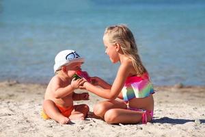 irmã feeds dela irmão em a de praia com Melancia. menina e pequeno Garoto estão comendo em a de praia. a crianças teve uma piquenique de a mar. foto