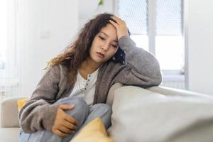 infeliz ásia mulher em sofá choro. solitário triste mulher profundo dentro pensamentos sentado sonhando acordado ou esperando para alguém dentro a vivo quarto com uma sério expressão, sentado em sofá foto