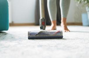 fechar acima foto do jovem mulher usando vácuo limpador limpeza tapete chão às casa
