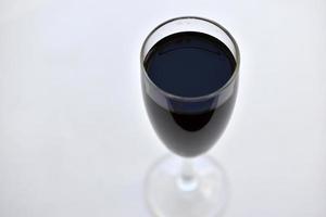 pequeno copo de vinho tinto em um fundo branco com sombras foto