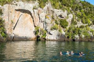 taupo, Novo zelândia - abril 24 2017 - turista natação dentro ótimo lago Taupo dentro frente do maori Rocha esculturas a icônico turista atração Lugar, colocar dentro lago taupo, Novo zelândia. foto