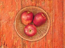 maçãs vermelhas em um prato de vime sobre um fundo de mesa de madeira
