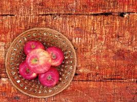 maçãs vermelhas em um prato de vime sobre um fundo de mesa de madeira