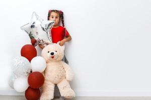 retrato do sorridente alegre menina brincando com Urso de pelúcia Urso dentro jogos sala. ela é fantasiando sobre ar balão foto