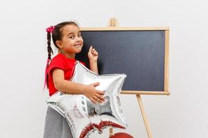 feliz brilhante imagem do fofa alegre pequeno menina dentro tule saia sentado em presente com balões isolado em branco fundo. surpreendente encantador aniversário elegante criança olhando para Câmera foto