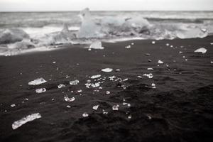 pequenos pedaços de gelo em praia de areia preta em vik, Islândia foto