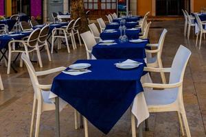 branco mesas com marinha azul toalha de mesa dentro restaurante esperando para clientes dentro Espanha foto
