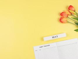 plano disposição do hábito rastreador livro, de madeira calendário poderia, e tulipas em amarelo fundo com cópia de espaço. foto