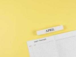 plano disposição do hábito rastreador livro, de madeira calendário abril em amarelo fundo com cópia de espaço. foto