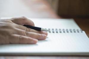 close-up de uma mão segurando uma caneta com um caderno foto