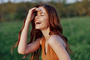 uma jovem mulher rindo e sorridente alegremente dentro natureza dentro a parque com a pôr do sol iluminação iluminador dela grandes vermelho cabelo foto