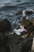descalço mulher deitado em rochoso costa com rachaduras em rochoso superfície Visão a partir de acima foto