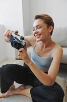 feliz sorrir mulher segurando a velho Câmera e levando As fotos do ela mesma Como uma final de semana fotógrafo dentro casa roupas com uma curto corte de cabelo cabelo sem filtros em uma branco fundo, livre cópia de espaço