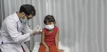 ásia médico injeção vacina para protegendo vírus covid-19 para uma menina vestem médico máscara, pessoas estão meninas estão vacinado contra gripe cada ano. foto