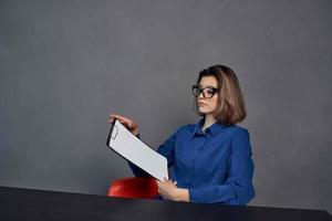 uma mulher dentro uma azul camisa senta às a mesa uma pasta dentro dela mãos documentos foto