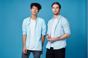 rapazes dentro idêntico camisas e uma camiseta em uma azul fundo amigos gesticular com seus mãos foto