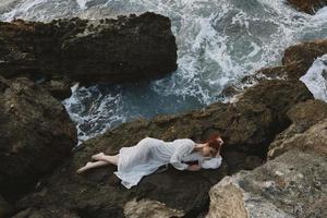 lindo mulher deitado em rochoso costa com rachaduras em rochoso superfície inalterado foto