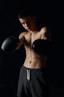 masculino fisiculturista com uma bombeado tronco dentro boxe luvas exercite-se Preto fundo foto