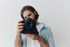 homem hipster fotógrafo dentro uma estúdio contra uma branco fundo segurando uma profissional Câmera e configuração isto acima antes tiroteio. estilo de vida trabalhos Como uma freelance fotógrafo foto