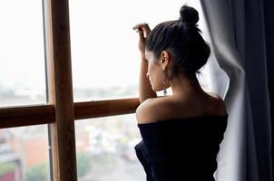 lindo mulher dentro uma Preto vestir perto a janela posando moda modelo foto