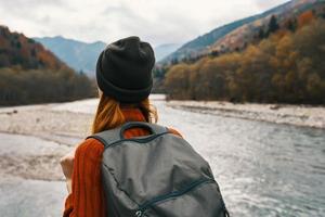 mulher dentro uma suéter boné com uma mochila em dela costas montanha rio dentro natureza foto