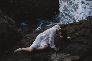 lindo jovem mulher dentro uma branco vestir deitado em uma pedra dentro uma branco vestir verão período de férias conceito foto