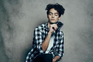 bonito masculino modelo dentro uma camisa e uma camiseta em uma cinzento fundo encaracolado cabelo Penteado Câmera estúdio foto