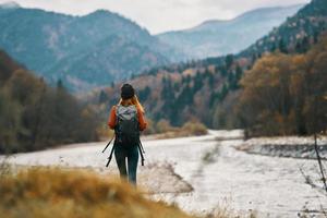 mulher viajante com uma mochila e dentro uma chapéu perto a rio dentro a montanhas dentro outono foto